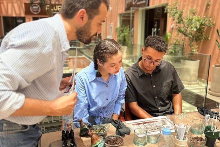 Three people at a table with various items including bottles, a menu, and a glass container. 1