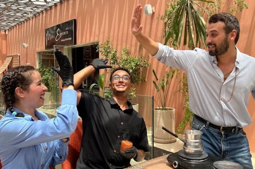 Three people in a courtyard with a coffee machine, a sign reading 'Moka Coffee,' and potted plants. 2