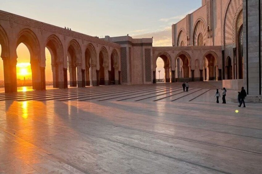 A large open courtyard with arches, a sunset, and people walking. 2