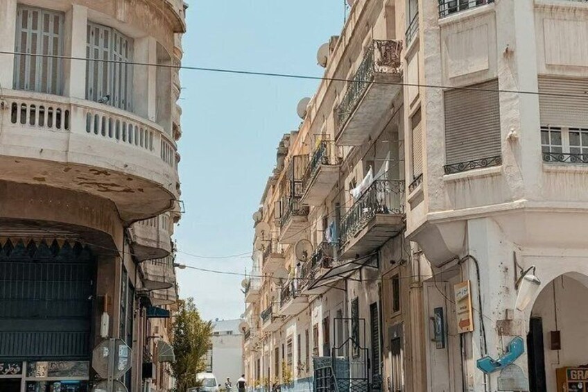 A narrow street flanked by multi-story buildings with balconies, a parked car, and a clear sky. 4