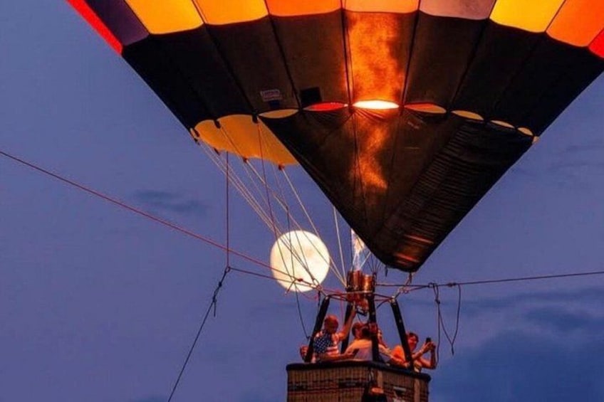A hot air balloon with a lit burner and a person on the basket against a twilight sky. 4