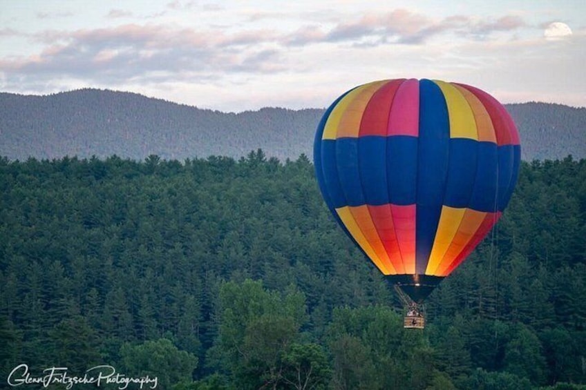 A colorful hot air balloon over a forested area with mountains in the background. 3