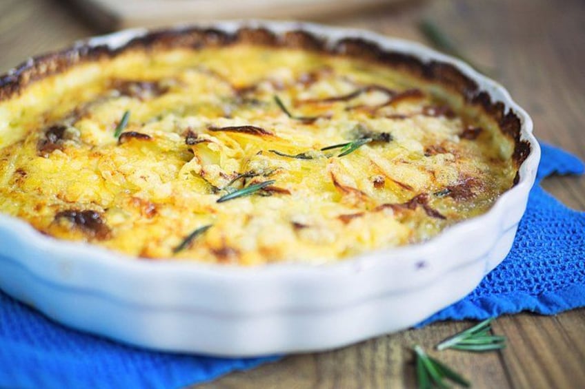 A quiche in a white ceramic dish on a wooden table with a blue cloth underneath. 4