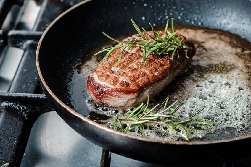 A cooked steak with a garnish of rosemary in a frying pan. 2