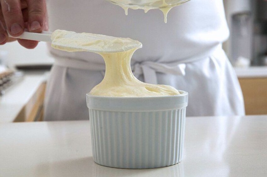 A person in a white apron scooping a creamy substance from a white bowl. 4