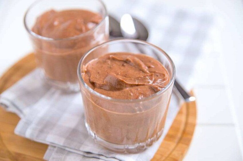 Two glasses of chocolate mousse on a wooden board with a spoon and a cloth napkin. 2