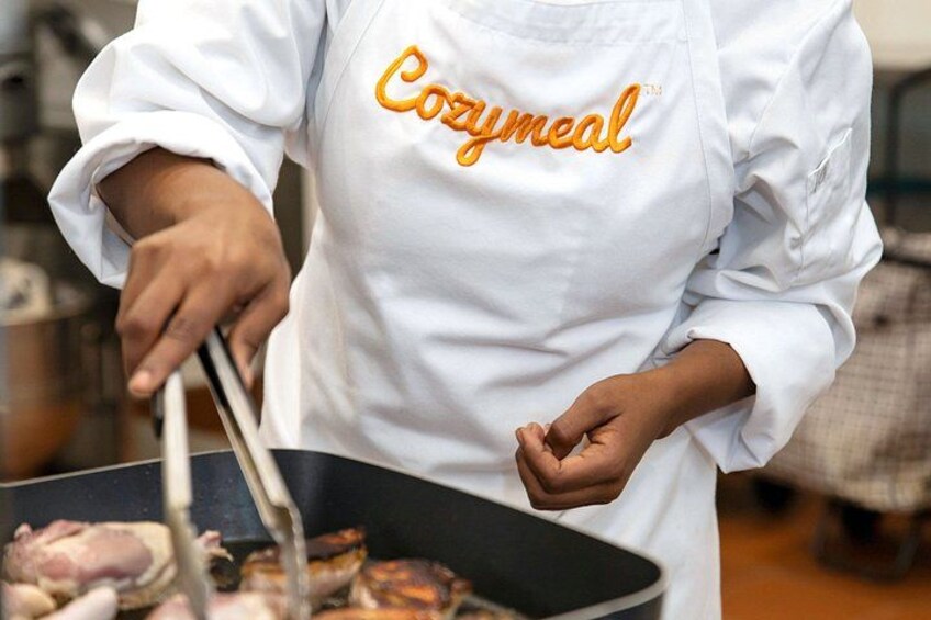 A person cooking with a pan, wearing a white apron with 'Cozymmeal' written on it. 5