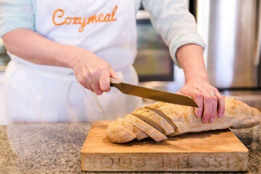 A person slicing a loaf of bread on a wooden cutting board. 3