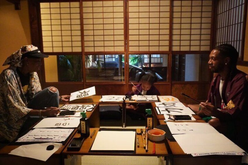 En grupp människor sitter runt ett bord med papper och skrivredskap i ett rum med traditionella japanska skjutdörrar. 3
