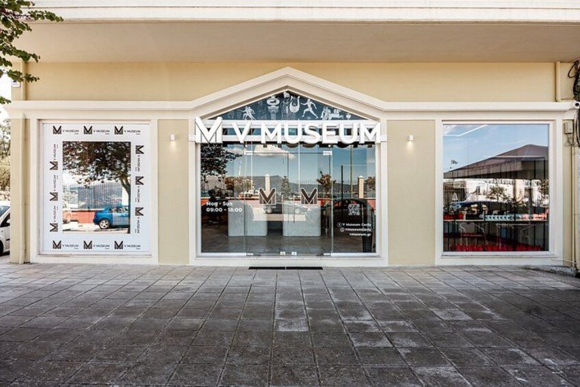 A museum entrance with a sign, a glass door, and a tiled pavement. 2