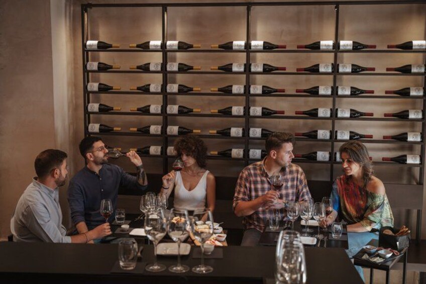 A group of people seated at a table in a wine cellar with wine bottles on shelves behind them. 3