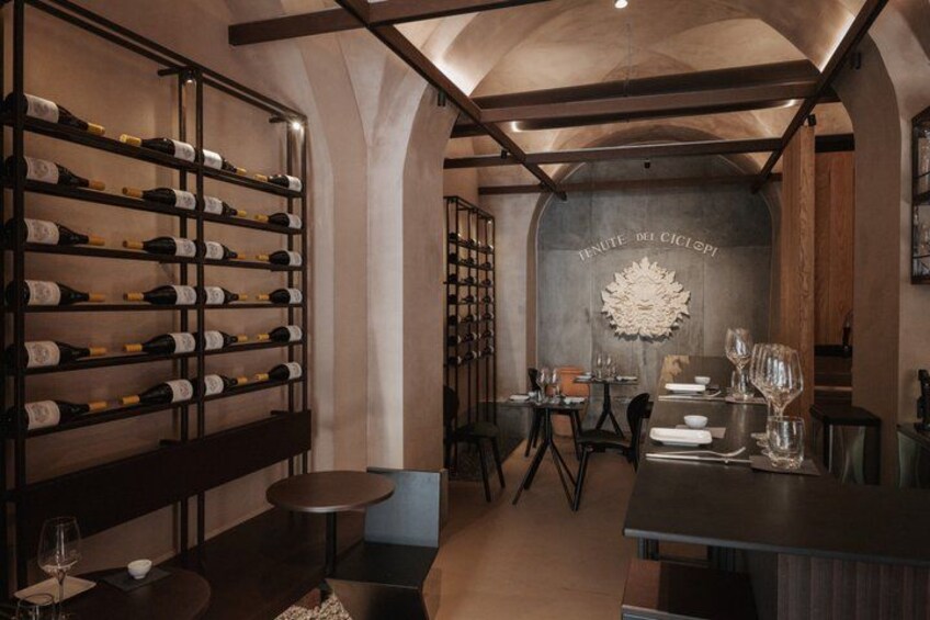 A wine cellar with shelves of wine bottles, a table set for dining, and a wall with a decorative emblem. 5