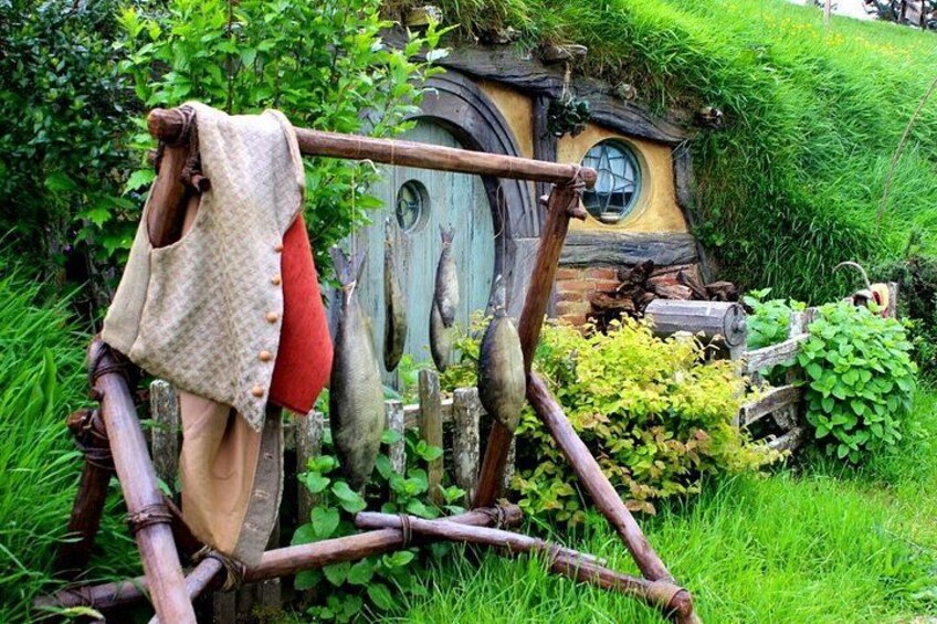 Ein Hobbit-Haus mit runder Tür, eine Holzkonstruktion mit einer Seilleiter und ein grüner, grasbewachsener Garten. 1