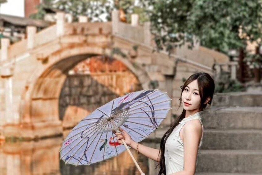 A person holding a decorative umbrella in front of an ancient stone bridge. 1