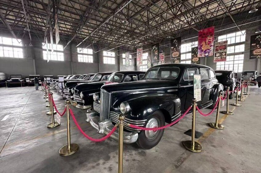A row of vintage cars on display in a museum with red ropes and gold stanchions. 4