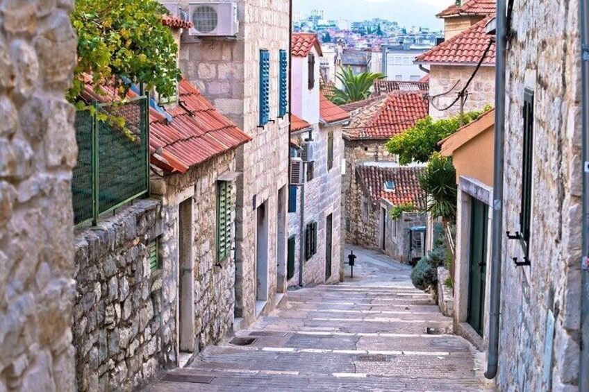 Un estrecho camino de piedra flanqueado por edificios con techos de tejas rojas y contraventanas verdes. 2