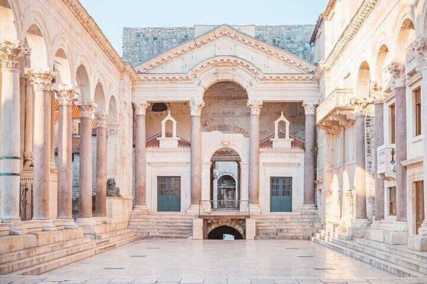 A historical building with classical architecture, featuring columns, arches, and a central staircase leading to an upper level. 1