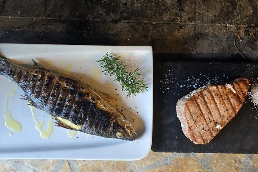 A grilled fish on a white plate with a sprig of dill, accompanied by a grilled meat on a black slate. 4