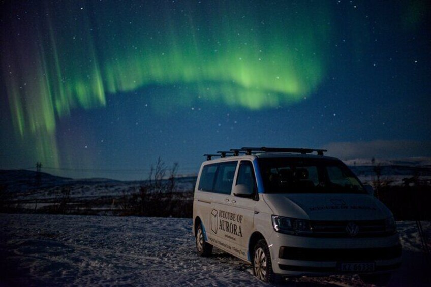 Una camioneta blanca estacionada en un paisaje nevado con la aurora boreal al fondo. 1