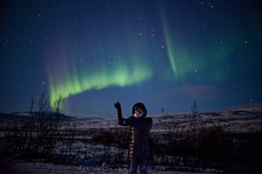 Una persona vestida de oscuro de pie en un paisaje nevado bajo un cielo nocturno con la aurora boreal. 4
