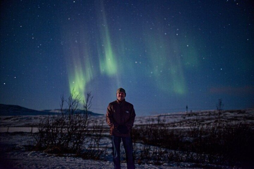 Una persona de pie en un paisaje nevado bajo un cielo nocturno estrellado con auroras visibles. 3