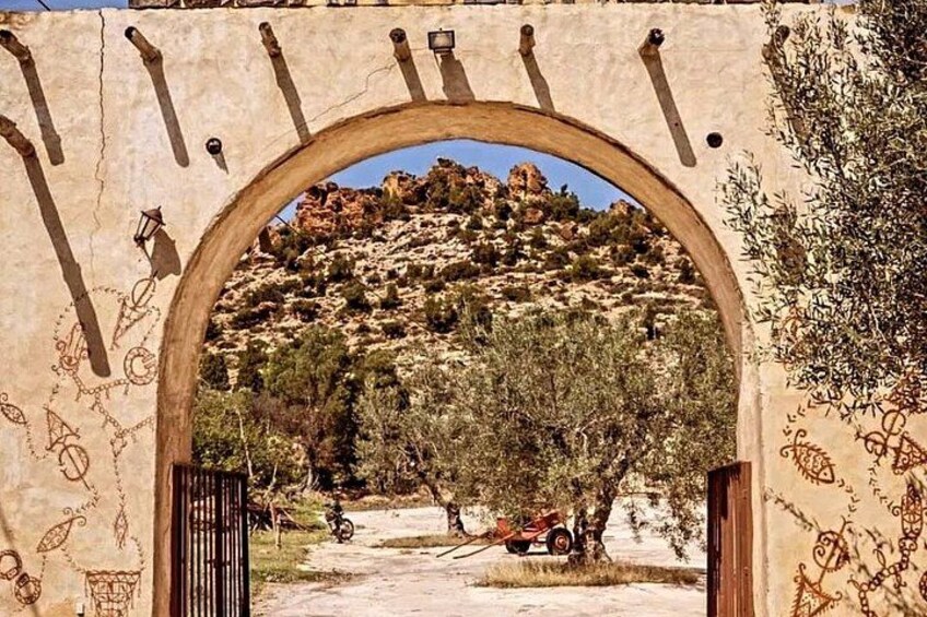 An arched doorway with a landscape view, a gate, and a wall with carvings. 1