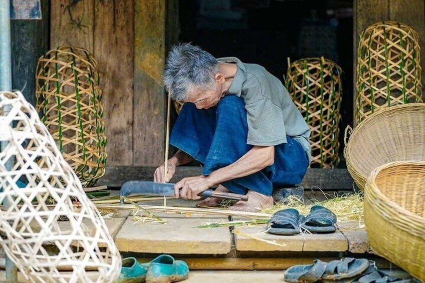 An elderly person weaving with a tool, surrounded by woven baskets and a pair of sandals. 2