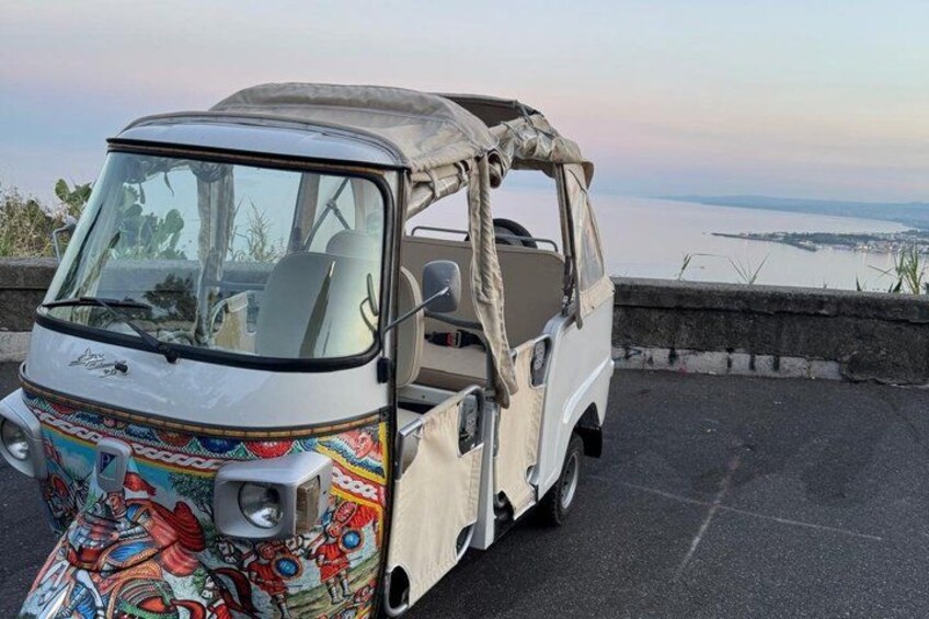 A three-wheeled vehicle parked on a road with a scenic view of a body of water and a bridge in the background. 3