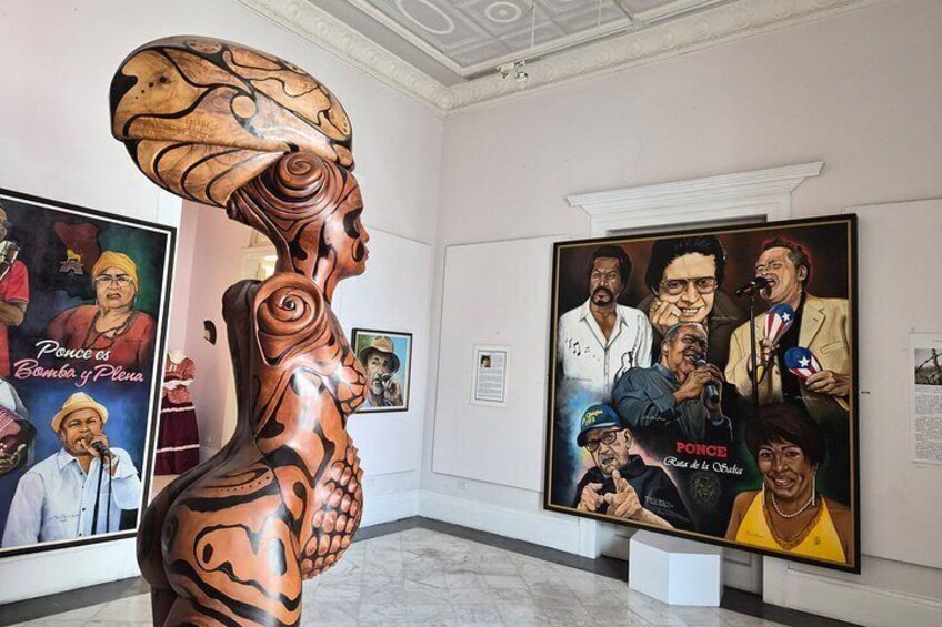 A sculpture of a human figure with intricate patterns, a framed poster with multiple portraits, and a marble floor. 2