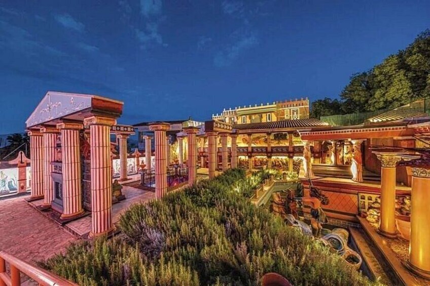 A well-lit architectural complex with columns, a garden, and a building with a tiled roof. 1