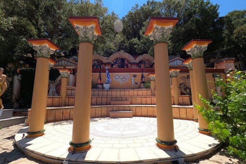 A circular plaza with columns, a central staircase, and a mural with Olympic symbols. 2