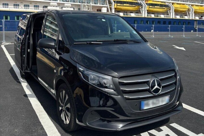 A black Mercedes-Benz SUV parked in an open area with a blue fence and yellow lifeboats in the background. 2