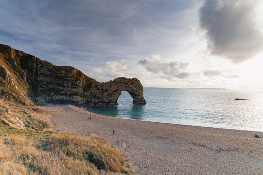 A coastal landscape with a prominent rock arch formation, a sandy beach, and a calm sea. 3