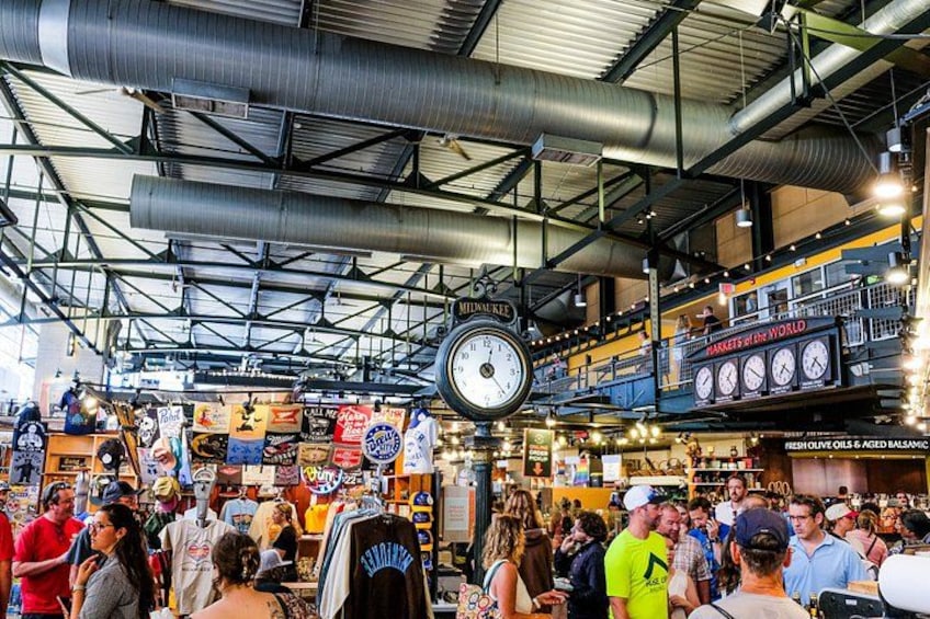 A busy indoor market with a large clock, various stalls, and a crowd of people. 5