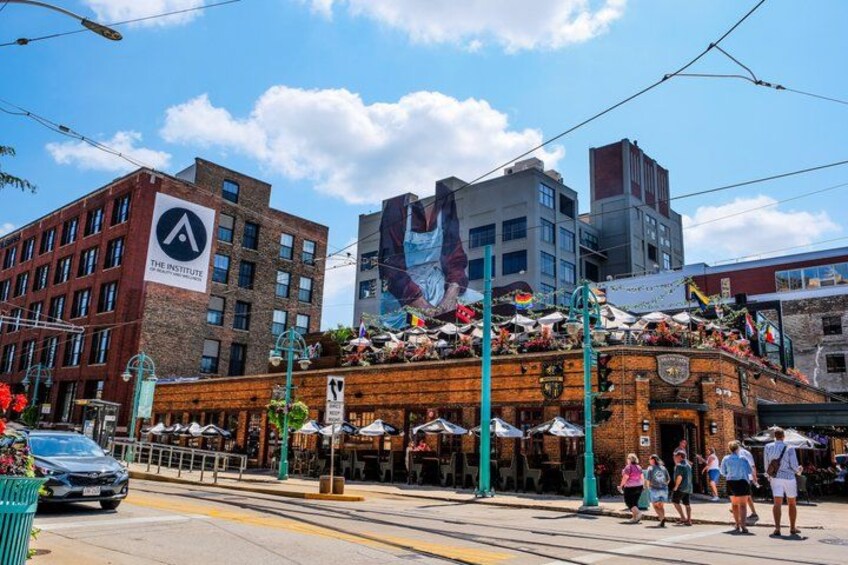 A street with a building featuring a large mural, outdoor seating, and a tram line. 4