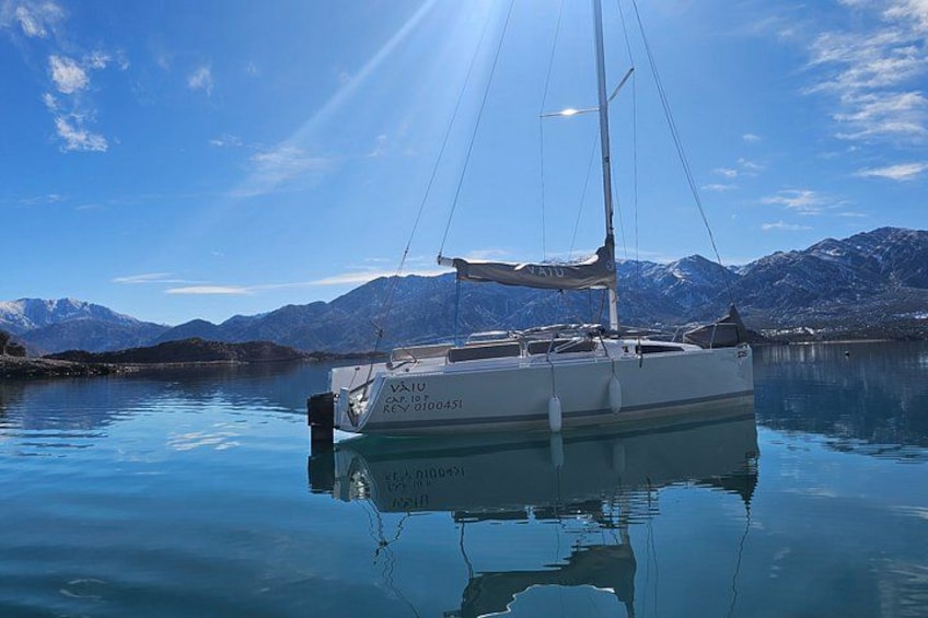 A sailboat anchored near a calm lake with mountains in the background. 2