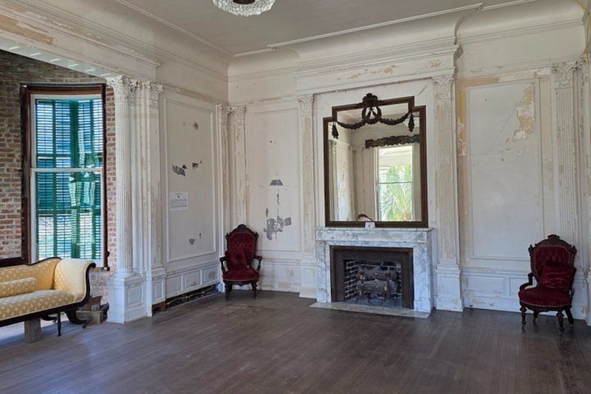 An empty room with a fireplace, two red chairs, a yellow sofa, and a large mirror. 3