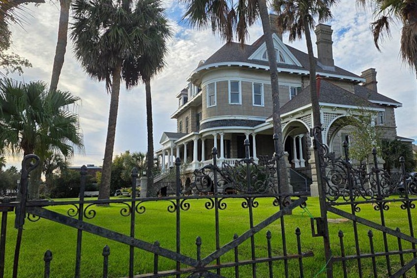 A large, historic house with a wrap-around porch, surrounded by a well-maintained lawn and palm trees. 4