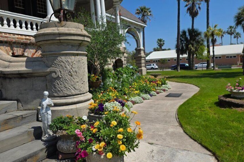 A well-manicured garden with a variety of colorful flowers, a stone statue, and a curved pathway leading to a building with a porch. 4