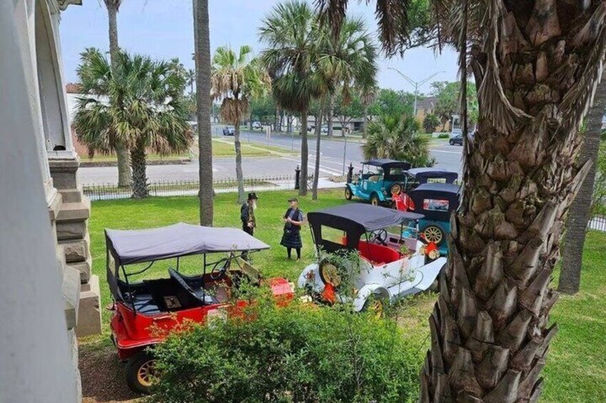 A red and white car with a canopy parked on a grassy area, palm trees, and a street in the background. 2
