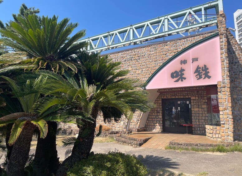 A building with a pink awning and a stone facade, under a metal bridge. 3