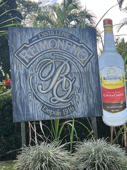 A wooden sign with the logo of Reimonenq and a bottle of their rum. 1