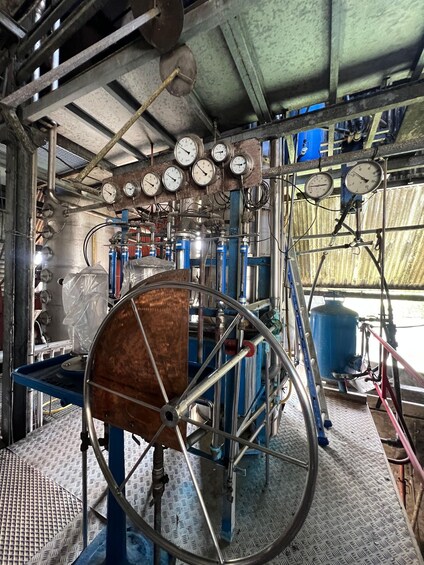 A mechanical room with industrial equipment, gauges, and a large copper wheel. 5