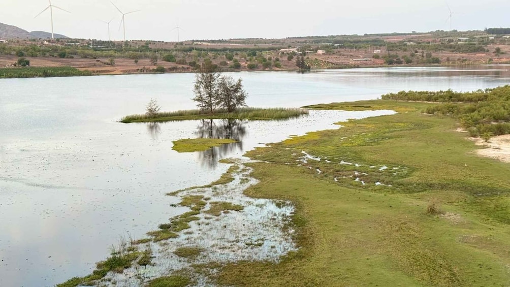A river with a grassy bank, a small island, and wind turbines in the distance. 2