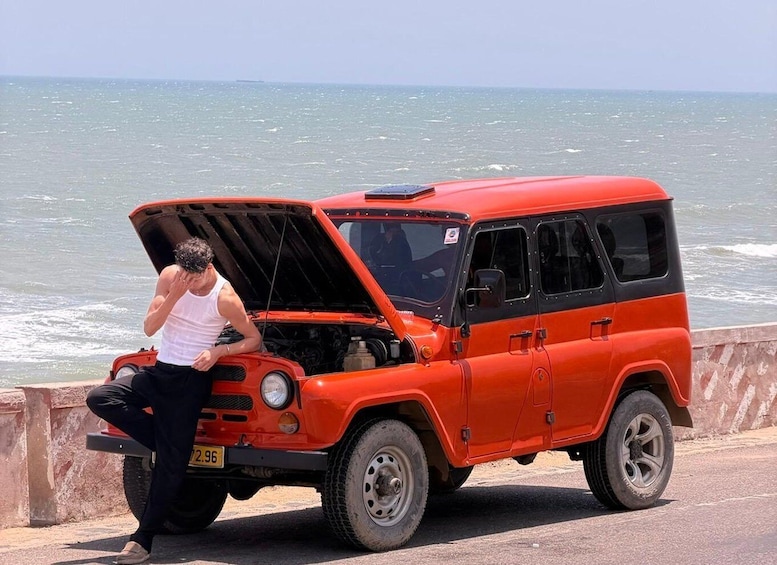 A red off-road vehicle with its hood open, parked on a concrete surface near a body of water. 4