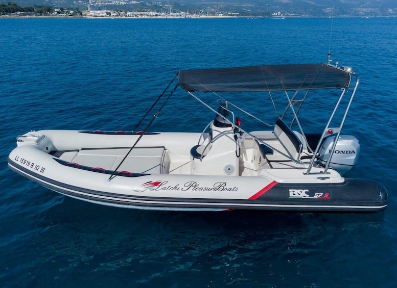 A white motorboat with a black canopy, branded 'Latchu Pleasure Boats,' on a calm blue sea. 2