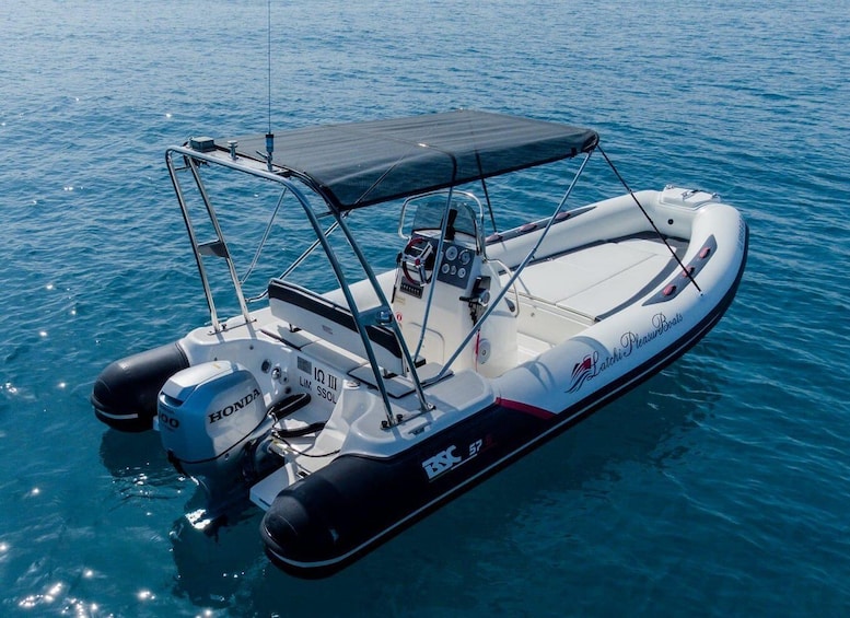 A white and black motorboat with a canopy, branded 'Latchi Pleasure Boats,' floating on calm water. 3