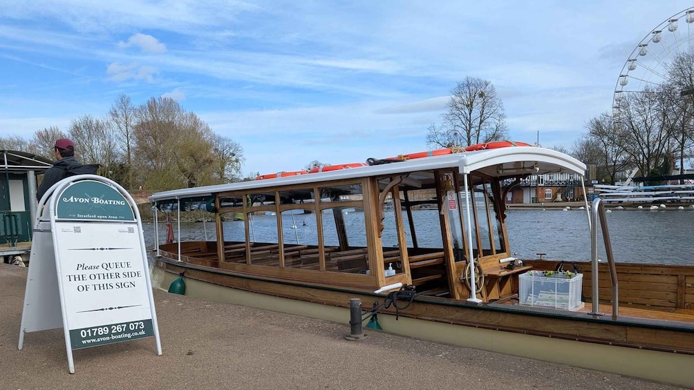 A wooden boat docked at a pier with a sign indicating to queue on the other side. 4
