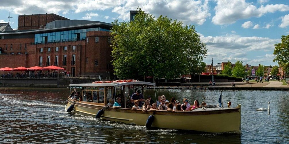 A boat with passengers on a river, a brick building, and a tree in the background. 3