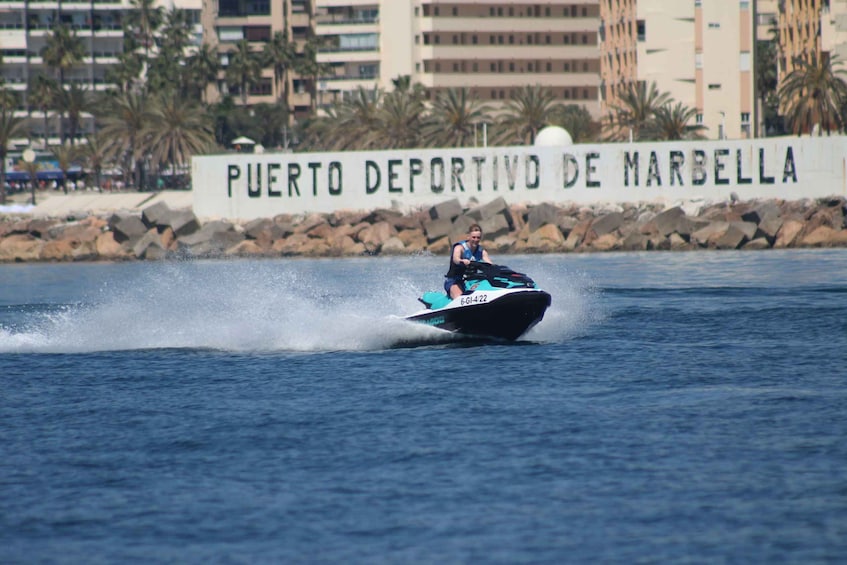 A jet ski on a body of water with a sign reading 'Puerto Deportivo de Marbella' in the background. 3
